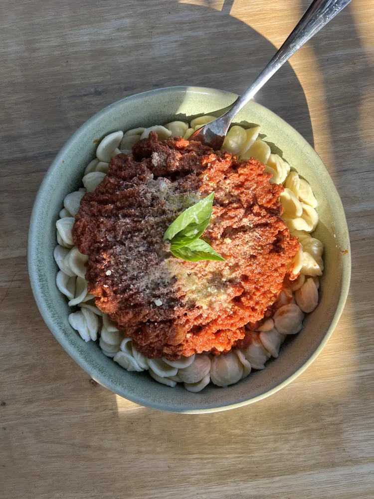 Bowl of orecchiette topped with bolognese, grated parmesan and a basil sprig